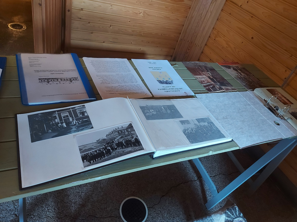 Pöytä, johon levitetty kirjoja ja lehtisiä. kirjoissa vanhoja kuvia sekä tekstejä, joissa kerrotaan rakennuksen historiasta