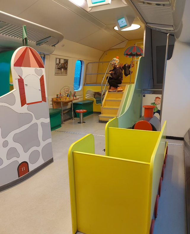 Kuvassa Suomen junissa oleva lasten leikkipaikka. kuvan keskellä, takana istuu lapsi rappusilla.