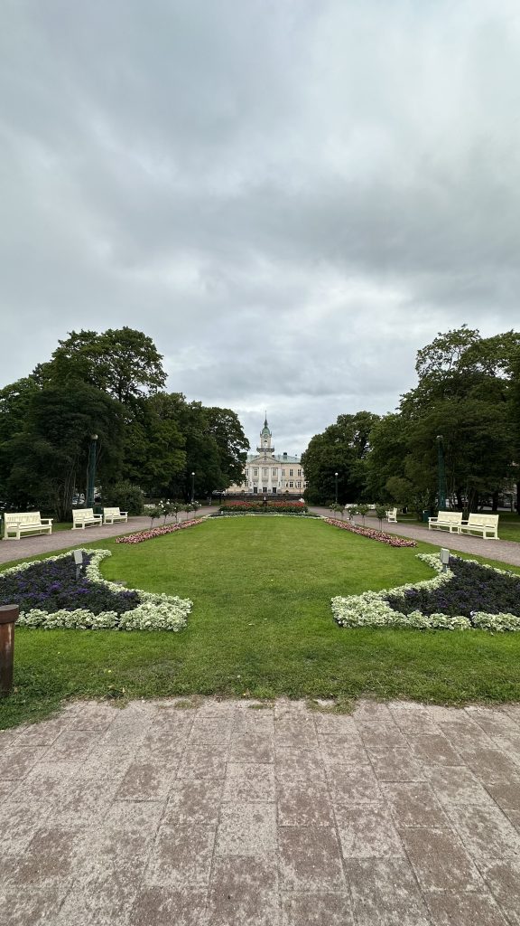 Green area of the park between the paths, paiving in the foregroud and Pori Old Town Hall in the backgroud.